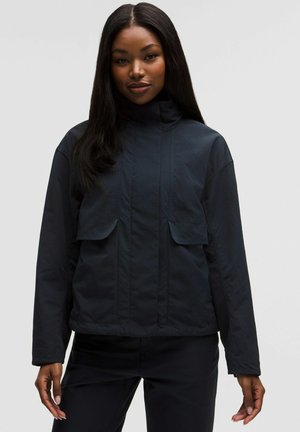 Dunkelmarineblaue, leichte Jacke mit hohem Kragen, zwei Vordertaschen und lockerer Passform. Glatte Textur mit dezentem Glanz.