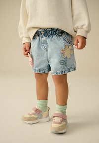 Shorts in denim di colore azzurro chiaro con cintura elastica, caratterizzati da una patch floreale e un dettaglio a forma di coniglio rosa, abbinati a sneakers pastello.