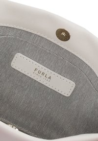 Interno di una borsa in pelle bianca con rivestimento in tessuto grigio, accessori in oro e un'etichetta con la scritta "FURLA SINCE 1927."