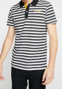 Musta-valkoraidallinen poolopaita, jossa on kontrastivärinen keltainen napillinen etulista ja pieni kirjailtu logo rinnassa. Lyhyet hihat.