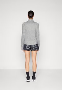Grå langermet topp med høy krage, kombinert med marineblå shorts med et lyst abstrakt blomsterdesign. Svarte sokker og sko fullfører antrekket.