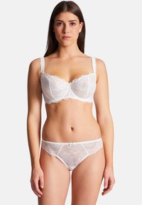 Soutien-gorge en dentelle blanche et thong assorti avec des motifs floraux, des bords festonnés et un petit nœud central ; design semi-transparent.