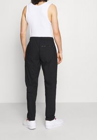 Schwarze, leichte Hosen mit einem elastischen Bund, seitlichen Taschen und einer mit Reißverschluss versehenen Gesäßtasche; kombiniert mit einem weißen Tanktop und Sneakers.