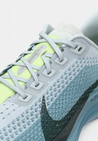 Tuva plāna gaismas zila Nike Pegasus skriešanas čizma ar sīki izstrādātu adījuma tekstūru, gaiši pelēkām auklām, neona dzeltenu mēli un melnu Nike swoosh logotipu.