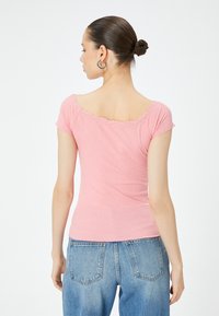 T-shirt in cotone rosa chiaro a coste con scollatura a scallop e maniche corte, abbinato a jeans in denim blu. La vista da dietro mostra un design aderente.