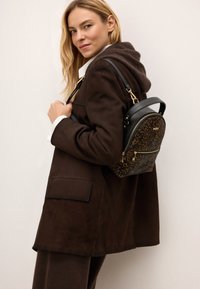 Musta ja pruun leopardimustriga mini seljakott, valmistatud nahast, ümar kuju, kuldse riistvara ja esimene tõmblukku tasku.