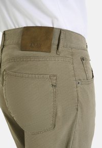 Lichtbruine, gestructureerde broeken met een vlak achterzak, een leren merklabel en subtiele stikdetails. Ontworpen voor comfort en functionaliteit.