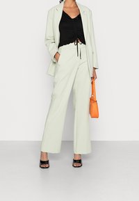 Completo su misura verde chiaro con pantaloni a gamba larga e un top nero aderente con dettagli arricciati. Accessoriato con una borsa a tracolla arancione dalla trama.