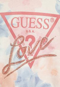 Bavlnené tričko s pozadím v pastelových akvarelových farbách. Obsahuje ružový trojuholníkový dizajn s nápisom "GUESS" a trblietavým "Love" v ružovom zlatom kamienkovom prevedení.