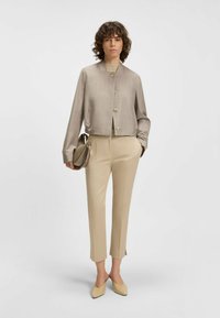 Kürz beige Jacke mit Knopfverschluss, kombiniert mit schmalen beigen Hosen und passenden Absätzen. Glatte Textur und maßgeschneiderte Passform.