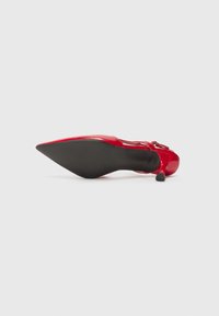 Red patent leather high-heel shoe with a pointed toe and black rubber sole. Features a slender heel and buckle accent on the straps.