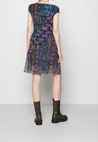 Mönstrad klänning med en blå och röd blommönster, korta ärmar och en utsvängd nederdel. Matchad med bruna ankelstövlar.