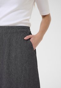 Grå denimkjol med en mjuk yta, med en bred midjeband och sidoficka. Buren med en vit åtsittande topp.