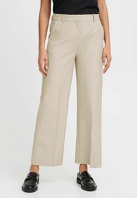 Beige wide-leg trousers with a textured fabric, flat front, and side pockets, paired with black loafers.