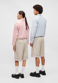 Ribade särgid punastes ja sinistes toonides, kombineeritud põlvepikkuste beežide lühikeste pükstega. Tekstuuriga kangas, nähtavad õmblused ja vastandavate mansettide aktsendid. Mustad kingad.