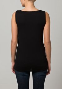 Black sleeveless top with a rounded neckline and a smooth texture. The hem is longer in the back, worn over dark blue jeans.