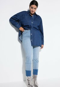 Übergroßes Jeanshemd mit zwei vorderen Taschen, Knopfleiste und einer hellen Waschung. Kombiniert mit hellblauen Skinny-Jeans mit einem dunkleren Saum.