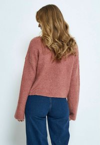 Rosa, flauschiger Pullover mit einem lässigen Schnitt und langen Ärmeln, ergänzt durch einen verkürzten Saum. Kombiniert mit navyblauen Schlaghosen.