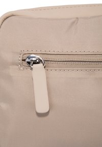 Sacchetto di tessuto beige con una superficie liscia, dotato di una cerniera argento e un battente della cerniera di colore chiaro su uno sfondo semplice.