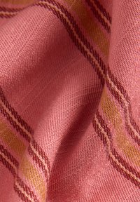 Tissu tissé en rose doux avec une texture fine, comportant des rayures diagonales en rouge foncé et jaune. Fini lisse, aspect léger.