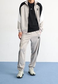 Idrottsdräkt i grått och svart, med en zip-up jacka och matchande byxor, med kontrasterande sidopaneler och logotypdetaljer.