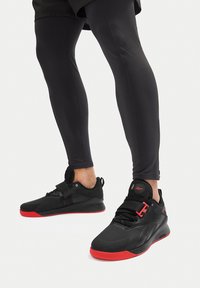 Czarne buty sportowe z czerwonymi akcentami, o smukłym designie, teksturowanymi overlayami i pojedynczym paskiem na środku stopy dla wsparcia.