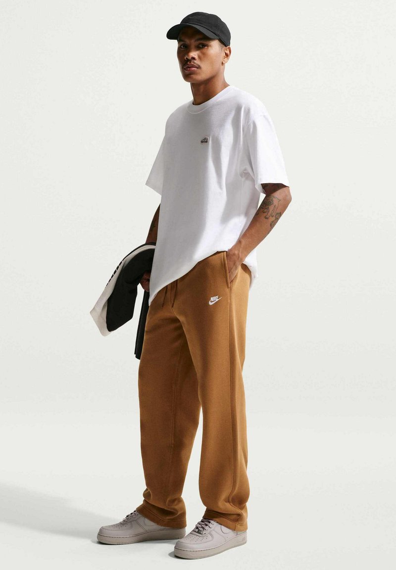 T-shirt blanc avec un petit logo, pantalon de survêtement marron avec détails de poches, et baskets gris clair. Comprend également une casquette noire et une veste noire.