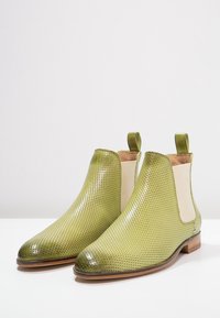 Botas Chelsea de cuero perforado verde con paneles laterales cremosos en contraste, puntas redondeadas y tacones bajos apilados.