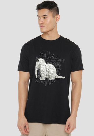 Black cotton t-shirt featuring a textured white graphic of a sitting animal with "I believe" text and starburst design elements.