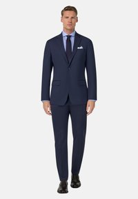 Mornarska obleka s prilagojeno silhueto, izdelana iz gladkega blaga, z dvojnim gumbom, zarezanim ovratnikom in hlačami brez nabora. Črne čevlje.