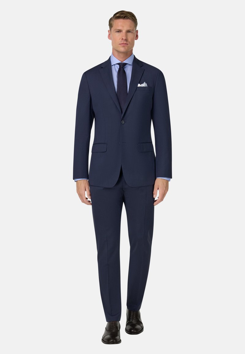 Mornarska obleka s prilagojeno silhueto, izdelana iz gladkega blaga, z dvojnim gumbom, zarezanim ovratnikom in hlačami brez nabora. Črne čevlje.