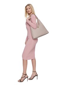 Borsa tote in pelle beige con logo dorato, abbinata a un vestito aderente rosa a coste e sandali neri con tacchi alti e lacci.