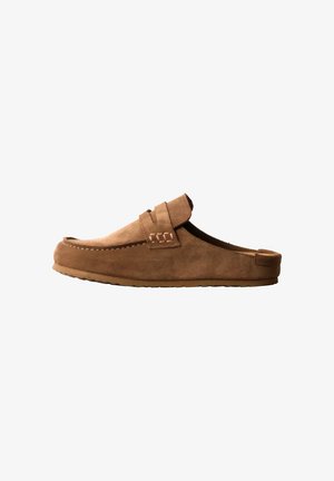 Mocassin marron en daim, sans lacets, avec une semelle en caoutchouc plate et une bride décorative sur le dessus, présenté de profil sur fond blanc.