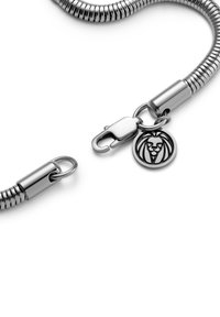 Metallarmband med flexibel design, med en silverfärgad yta, låsning med clasp och en rund berlock med lejonemblem.