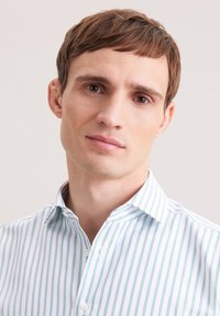 Hellblau-weiß gestreiftes Hemd mit Knopfkragen, aus einem hochwertigen Stoff mit schmalen Streifen. Nahaufnahme von Kopf und Schultern eines Mannes.