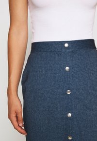 Denimkjol med ett åtsittande midjeband, silver knappstängning framtill och en medelblå färg med ett strukturerat tyg.