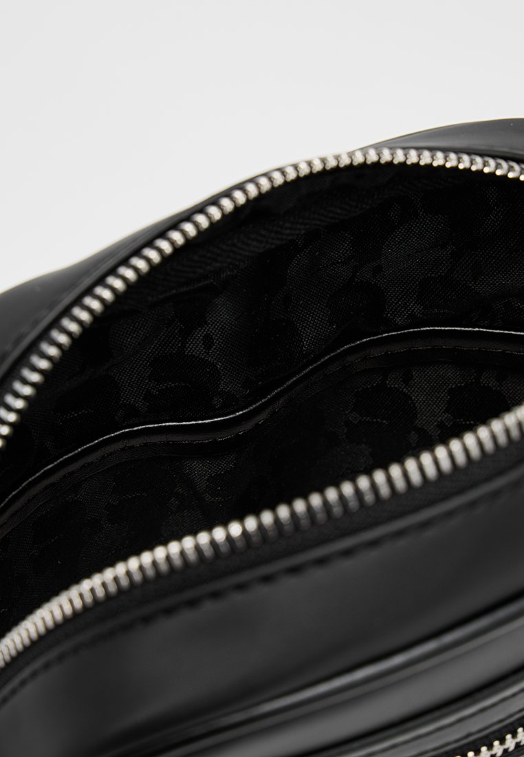 Bolsa de cuero negro con cremallera plateada parcialmente abierta, que muestra un forro interior de tela negra con estampado.