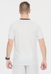 Valkoinen urheilupaita lyhyillä hihoilla ja mustalla pyöreällä kaula-aukolla, valmistettu sileästä, hengittävästä kankaasta, säännöllisessä mitoituksessa ilman kuvioita.