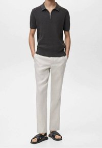 Polo gris foncé à manches courtes avec un col zippé, associé à un pantalon beige clair et des sandales noires à enfiler, mettant en valeur une texture lisse.