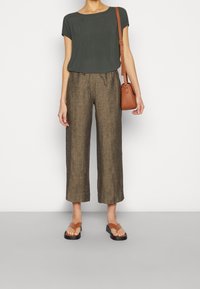 Top corto verde scuro a maniche corte, pantaloni larghi in lino marroni con gambe corte, borsa marrone e sandali piatti con suola nera spessa.