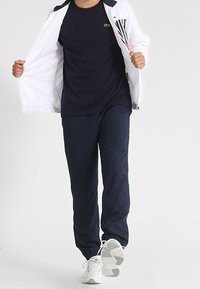 Camisa atlética navy, chaqueta blanca con rayas y pantalones navy a juego. Zapatillas deportivas blancas, ajuste casual, tejido ligero.