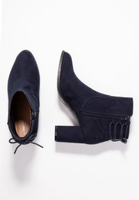 Granatowe zamszowe botki za kostkę z blokowym obcasem, zapinane na zamek z boku, z koronkowym detalem z tyłu. Gładka faktura z wzmocnionymi szwami.