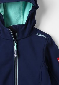Navy blue children's jacket with a turquoise fleece lining and hood, featuring a front zip closure and logo detail on the shoulder.