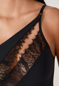 Bañador negro con inserción de encaje con patrones intrincados, tirantes ajustables y un diseño ajustado y elegante. Textura suave en toda la prenda.
