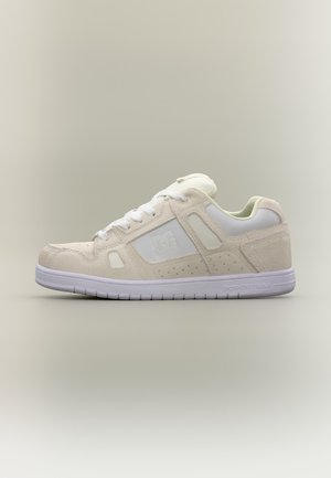 Baskets basses beige et blanches avec lacets blancs, panneaux latéraux perforés et semelle blanche arborant le logo DC Shoes sur le côté et le talon.