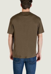 Maglietta verde oliva, maniche corte, realizzata in cotone, con collo rotondo e una texture liscia. Indossata con jeans blu.