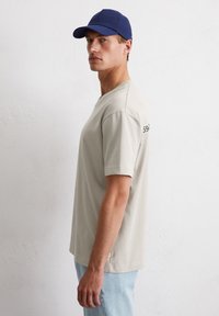 Lichtgrijs T-shirt met korte mouwen en een ronde hals, gecombineerd met een donkerblauwe pet. Eenvoudig ontwerp, ontspannen pasvorm, geen patronen of graphics.