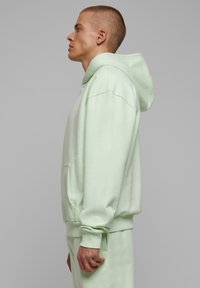 Sudadera verde menta de tela suave, cuenta con un bolsillo tipo canguro, puños acanalados y un corte relajado con capucha ajustable.