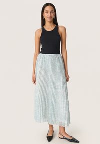 Sort ribbet tanktop parret med en lyseblå plisseret maxiskirt. Skirtet har et subtilt mønster, og modellen bærer sorte spidse flade sko.