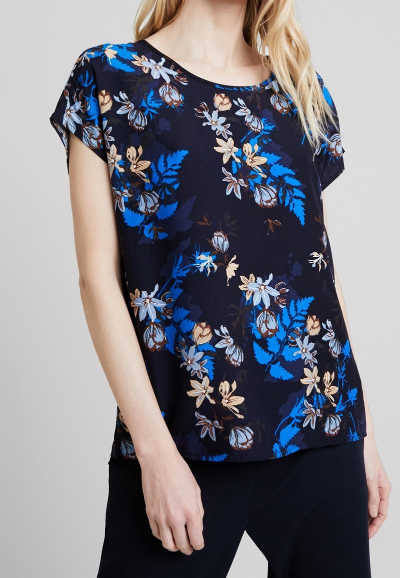 Bluse mit kurzen Ärmeln in Marineblau, verziert mit Blumenmustern in Blau, Weiß und Braun. Aus weichem Stoff mit lockerer Passform gefertigt.